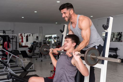A hispanic gym instructor teaching a young student how to train with a barbell in a gym