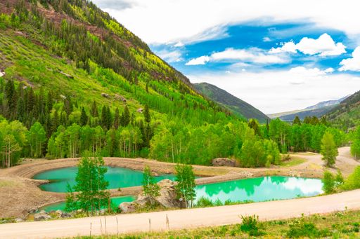 A scenic landscape of a forest on the hill with an emerald green pond and a cloudy sky above in Telluride, CO