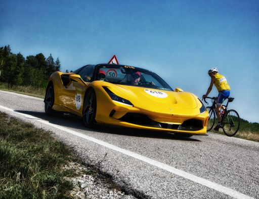 A yellow Ferrari F8 Spider IN an old racing car in rally Mille Miglia 2022 with a bicyclist nearby