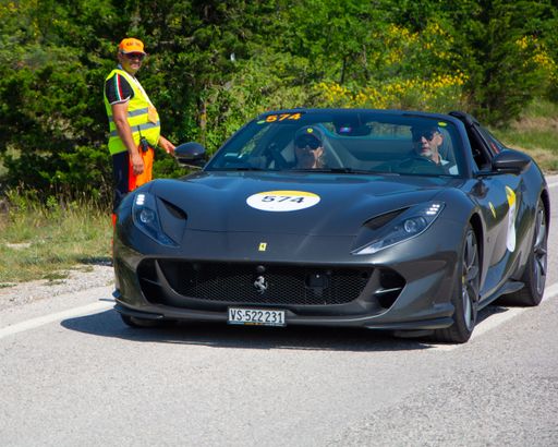 A black Ferrari F8 Tributo IN an old racing car in rally Mille Miglia 2022 with a police officer nearby