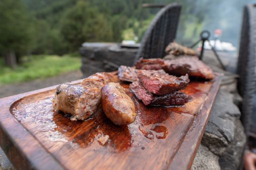The tasty cooked barbecue meat slices and sausages on a wooden board in the garden
