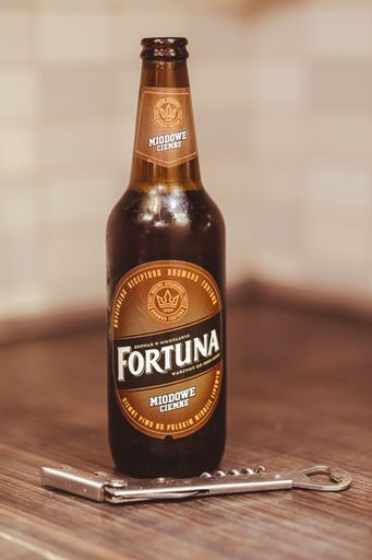 A vertical shot of a Polish Fortuna brand beer with honey and a bottle opener on a wooden table
