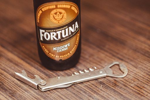 A closeup shot of a Polish Fortuna brand beer with honey and a bottle opener on a wooden table