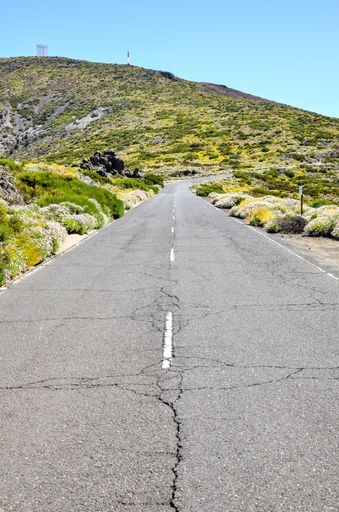 A vertical shot of highway road surrounded by shrubby hills captured on a sunny day