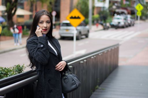 A young beautiful female in a black coat and heels talking on the phone outdoors