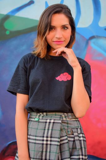 The white young woman wearing a casual outfit posing for the camera while standing against the graffiti wall, vertical