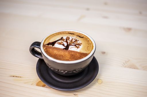 A closeup shot of a cup of Sunset tree latte art coffee on a wooden table