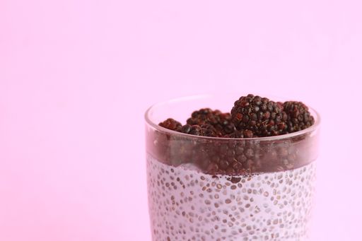 A closeup of a glass of chia pudding with blackberries against a purple background