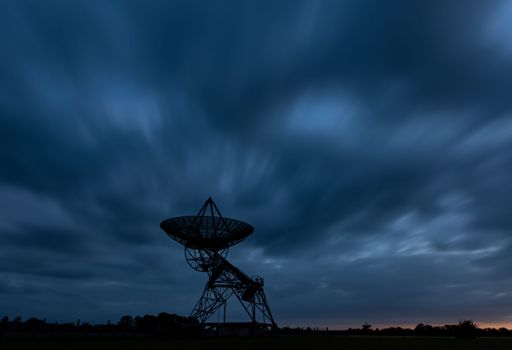 A silhouette shot of a radio telescope dish on a field during dusk
