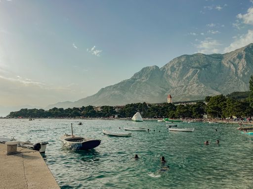 A beautiful shot of boats and some people in a water with a mountainous landscape in the background