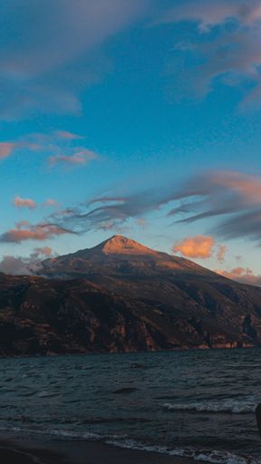 A vertical shot of a mountain under the colorful cloudy sky during the sunset