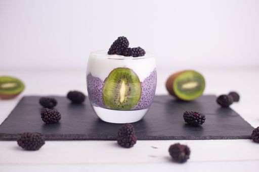 A closeup of chia pudding with blackberries and kiwis on a board under the lights