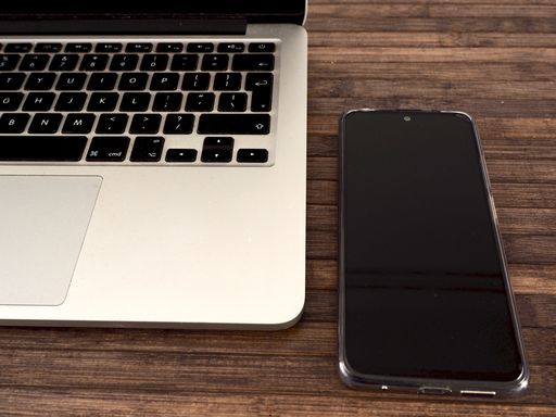 A closeup shot of a silver laptop and a smartphone on a brown table