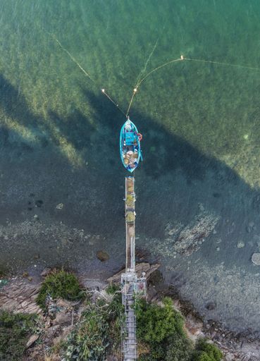 A top down aerial view of a boat moored to a dock