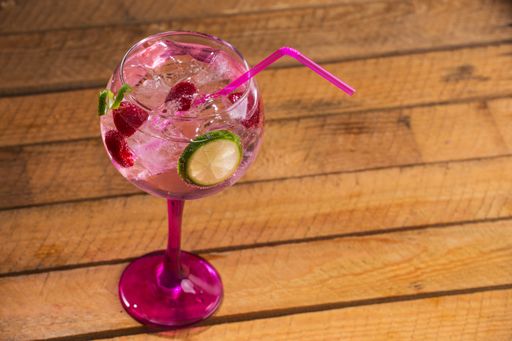 A closeup shot of a fresh cold cocktail with ice cubes and a slice of lime on a wooden surface