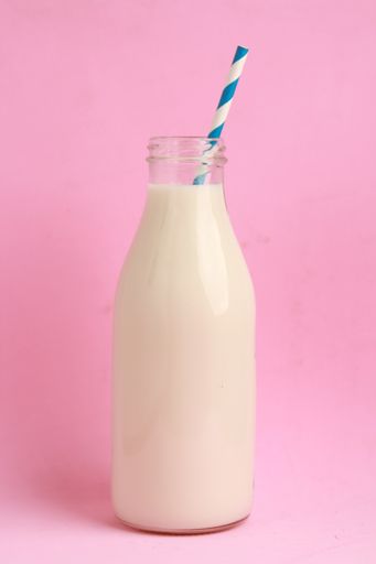 A closeup shot of milk in a glass bottle against a pink background