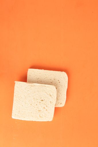 A vertical high angle closeup shot of two bread slices without rind on an orange background
