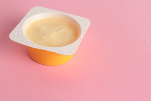 A closeup shot of custard in a plastic container on a pink surface