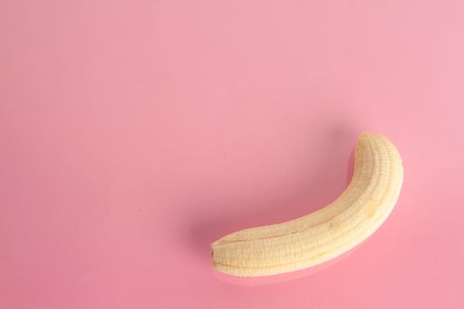 A high angle shot of a peeled banana isolated on a pink surface