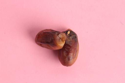 A high angle shot of two dry dates isolated on a pink surface