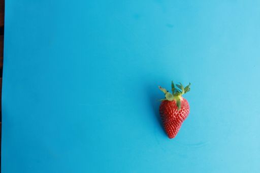 A high angle shot of a fresh strawberry isolated on a blue surface