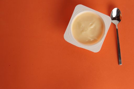 A high angle closeup shot of yogurt and a spoon on an orange background