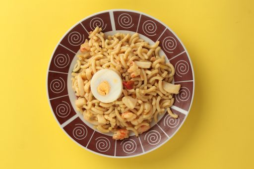A top view of seafood macaroni pasta and boiled egg on yellow background