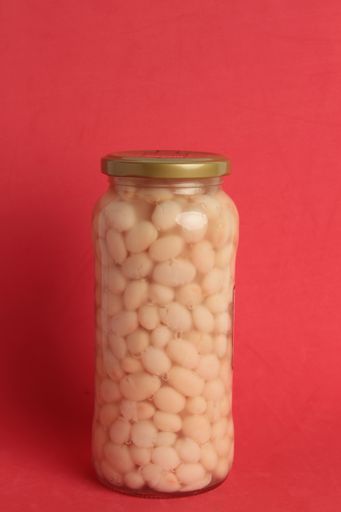A vertical shot of a jar filled with cloves of garlic isolated on a pink background