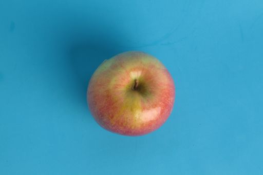 A top view of a whole apple under the lights isolated on a blue background