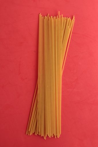 A vertical shot of raw spaghetti on a pink background