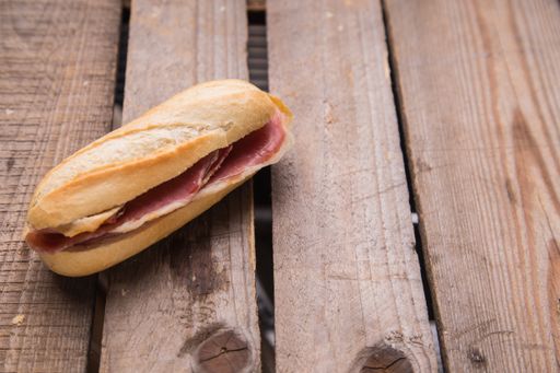 A closeup shot of serrano ham sandwich on a wooden surface