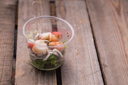 A high angle shot of a plastic bowl with vegetables and seafood on a wooden surface