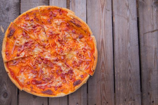 A top view of a homemade pizza with cheese and ham on a wooden table