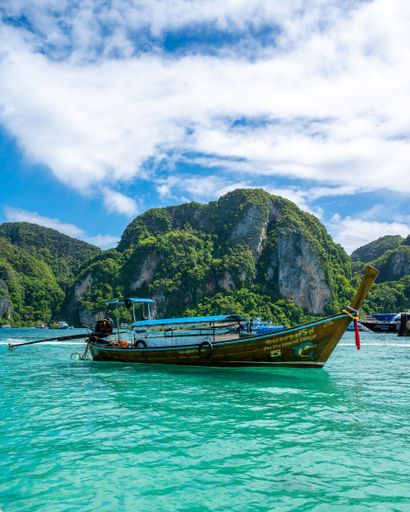A vertical shot of a boat on the blue water of the ocean surrounded by cliffs