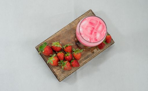 a top view of a strawberry milkshake in a glass and fresh strawberries around on a wooden board