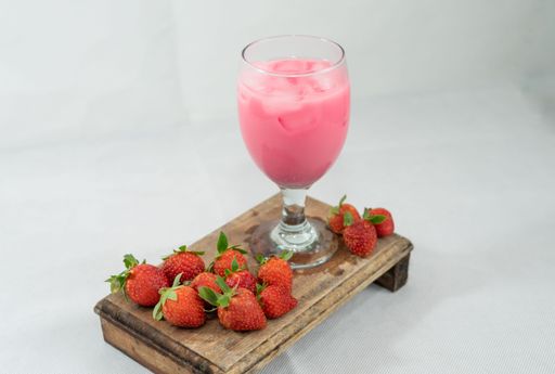 a shot of a strawberry milkshake in a glass and fresh strawberries around on a wooden board