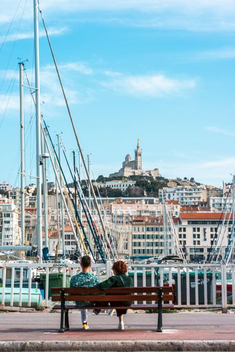 a vertical shot of a couple sitting on a bench near the old port of marseille