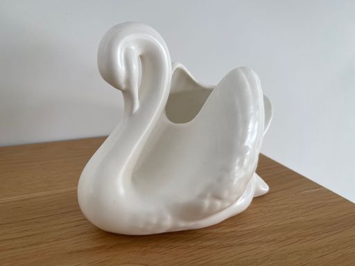 A ceramic ashtray in the form of a white swan on a wooden table