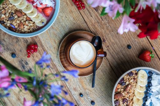 A top view of a cup of cappuccino and smoothie bowls with granola