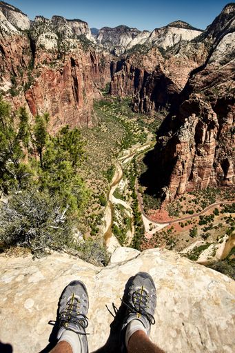 A sunny scenery of a traveler sitting on a rocky edge the Angels Landing Trail in Zion National Park