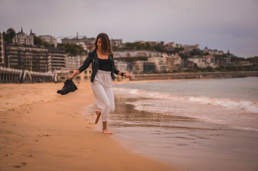 A young stylish female walking barefoot on a beach at sunset holding her shores