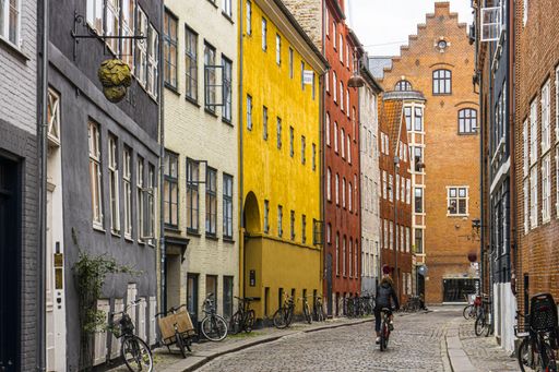 The image shows one of the oldest streets in the city of Copenhagen with 3 or 4  story buildings lining both sides with bicycles on both sides