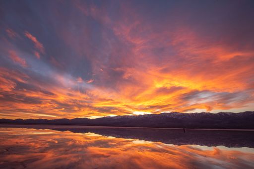 A mesmerizing scene of dramatic orange cloudy sky reflect on lake water in Badwater Basin, California