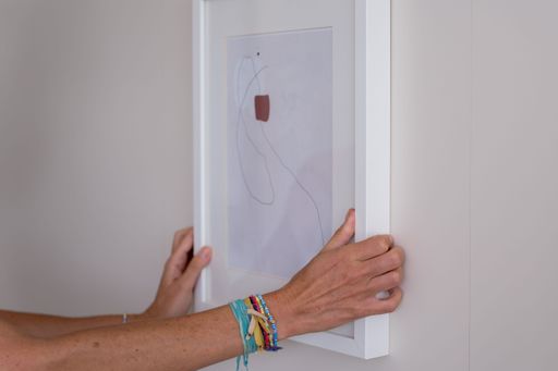 The hands hanging an abstract framed painting on the gray wall