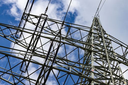 A closeup shot of a powerline with electric wires against a blue sky on a sunny day