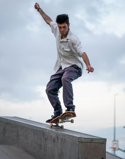 A vertical shot of a European male jumping on a skateboard in a skate park