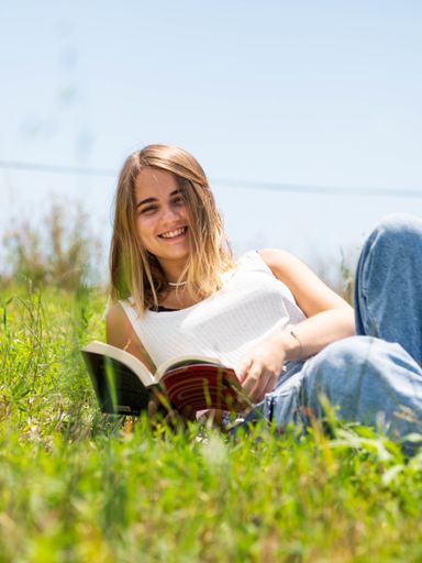 A vertical shot of a blonde Caucasian woman reading a book in the park