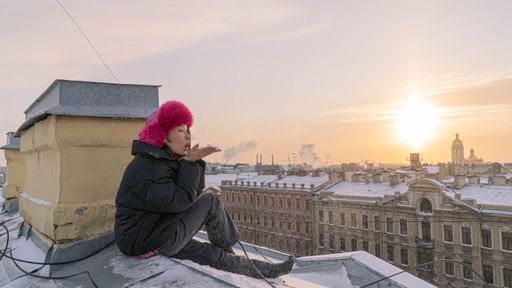 A girl in winter outfit sitting on the rooftops in Saint Petersburg enjoys the sunrise