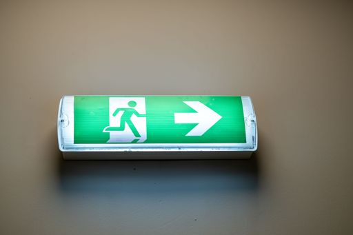 A green emergency light sign on a wall showing a direction with a white arrow