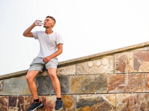 A young Caucasian man resting and drinking water after an outdoors workout